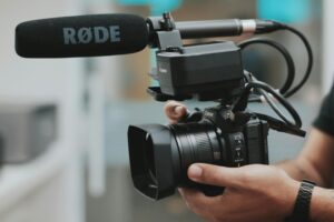 Close-up of hands holding a professional video camera with a RØDE microphone attached.